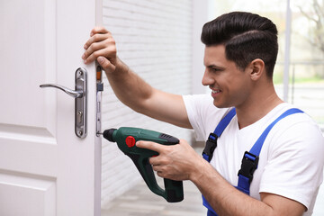 Handyman with screw gun repairing door lock indoors