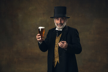 Elderly gray-haired man, gentleman, aristocrat or actor drinking beer isolated on dark vintage background. Retro style, comparison of eras concept.
