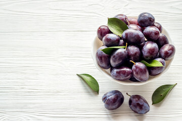 Ripe garden plums in bowl. Cherry fruit with leaves. Top view