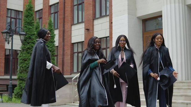 Happy graduates of a university or college of African American nationality in square robes throw up square hats of the master upwards. Student exchange program. Higher education for women in Europe