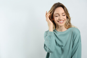 Portrait of happy young woman with beautiful blonde hair and charming smile on light background. Space for text