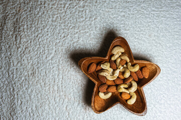 cashew nuts and almonds in a beautiful wooden bowl in the shape of a star on a white background