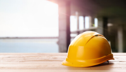 Hard hat on wooden surface at construction site with unfinished building. Space for text