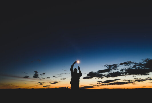 man against the sunset with a glow in the hands, dark sky with stars