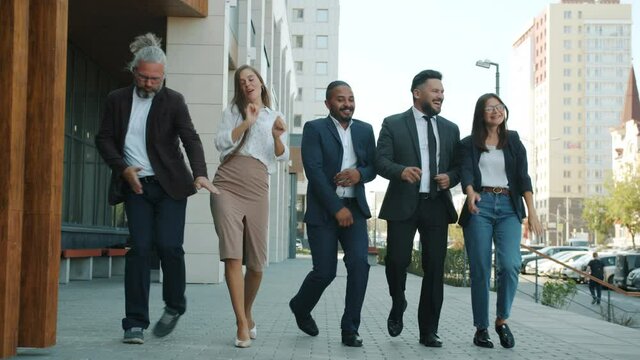 Multi-ethnic corporate team men and women are dancing and walking outdoors in business district. Positivity and successful businesspeople concept.