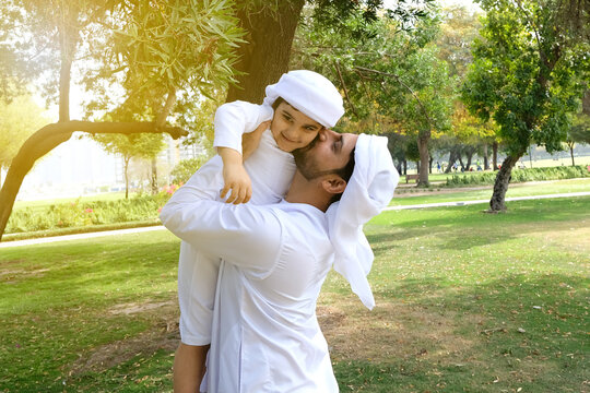 Arab dad kisses his child as family love affection. Arabic young kid model smiling with his Arabian father in the Middle East both wearing white dress Dish Dash Kandura