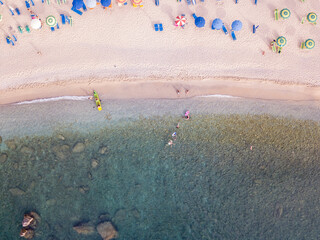 Aerial view of a beach and umbrellas. Tropea, Calabria, Italy.  Parghelia. Overview of seabed seen from above, transparent water. Swimmers, bathers floating on the water. Beach and rocks of Vardanello
