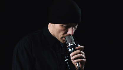Male musician singing into a microphone. Shot on a black background. Dark atmosphere.