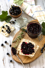 Blackcurrant jam in a glass jar and gluten-free crispbread on a rustic table.