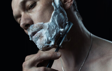 man shaves with an old dangerous razor on a dark background