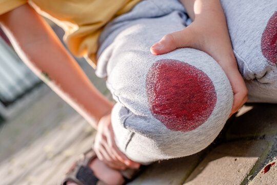 Shot of a young child with a knee injury on the street during the day. Photo of boy holding his knee while falling in sidewalks