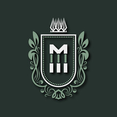 Vintage premium monogram of letter M. Heraldic coat of arms in form of shield surrounded by floral ornament and crown.