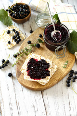 Blackcurrant jam in a glass jar and gluten-free crispbread on a rustic table. Copy space.