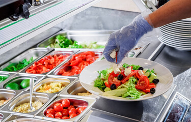 Chef prepares salad at the salad bar. Salad making process. Showcase salad bar with an assortment of ingredients for healthy and dietary food. High quality photo