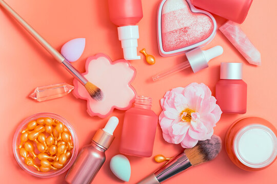 Cosmetic products, top view. Pink bottles and tubes with dispensers, powder, blush, anti-aging ampoules of youth, brushes, cream, essence