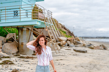 Cute young woman on a beautiful beach with a blue lifeboat in San Elijo State Beach, San Diego