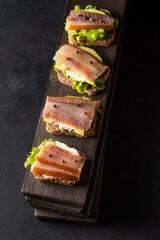Sandwiches with smoked fish on a board on a dark background.