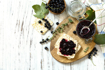 Blackcurrant jam in a glass jar and gluten-free crispbread on a rustic table. Top view flat lay background. Copy space.