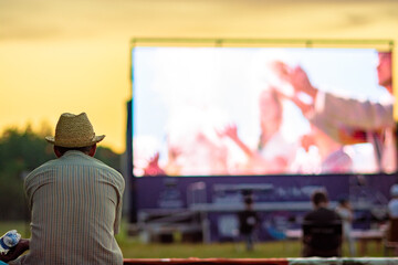 Summer cinema. A man in a straw hat is watching a movie in the open air.