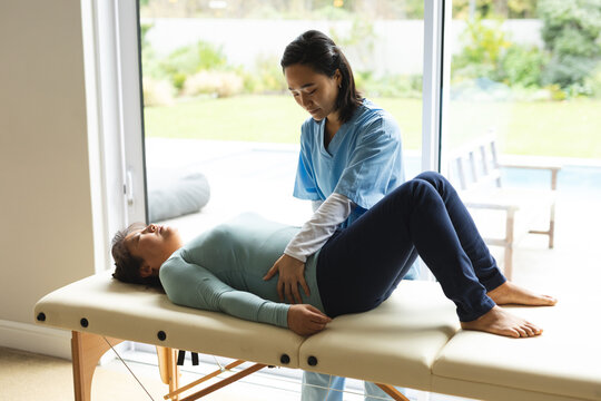 Asian female physiotherapist treating senior female patient at her home