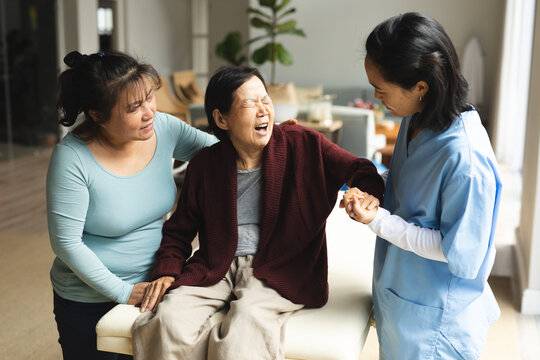 Asian female physiotherapist and daughter treating senior female patient at her home
