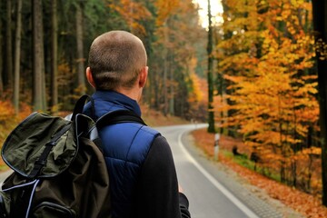 Traveler with a backpack  walks along the road in the autumn forest.Autumn hikes.Walking and hiking in the fall.Beautiful autumn nature view. Autumn season. Autumn mood