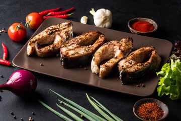 Pieces of grilled carp on a plate with tomites, peppers, red onions, garlic