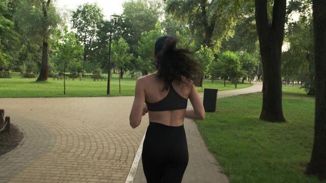 Young fitness woman jogging outdoor. Female runner training in summer park. Focused female athlete runner