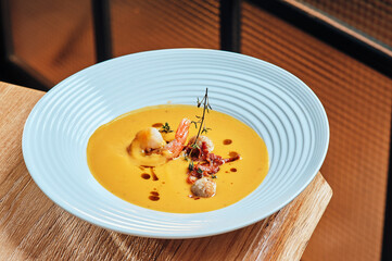 Pumpkin cream soup with fried shrimps in a beautiful plate on a wooden background. Healthy organic food concept. Space for text. High quality photo