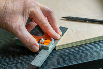 selected focus of a caprpenter marking out a perfect forty five degree angle on a piece of plywood using an adjustable calibrated square and a mechanical pencil