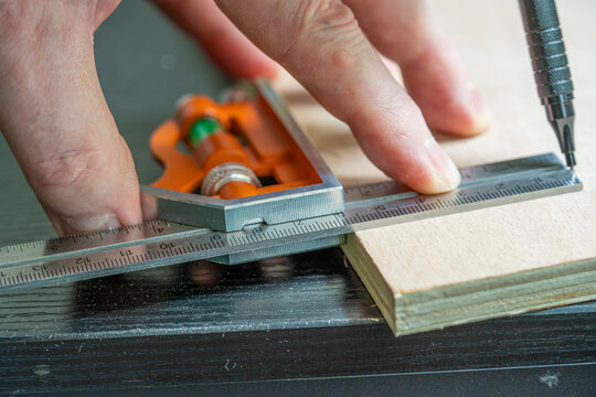 selected focus of a caprpenter marking out a meaurement on  a piece of birch plywood using an adjustable calibrated square and a mechanical pencil