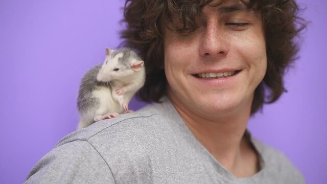 Close-up of a young guy with curly hair smiling at the camera on an isolated background, a pet rat is sitting on his shoulder