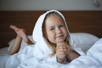 portrait of a little girl in a robe lying on the bed in the bedroom