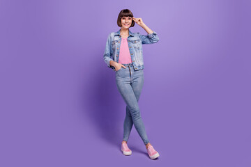 Full size photo of millennial brunette lady stand wear spectacles jeans shirt sneakers isolated on purple background
