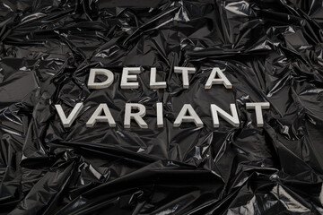 words delta variant laid with silver metal letters on crumpled black plastic bag background