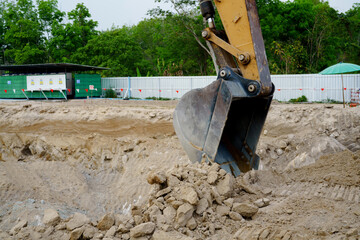 A large yellow backhoe is planting and grading brown rays in a factory construction area.