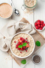 Oatmeal porridge with fresh raspberries, strawberries and red currants on a white background. Top view, close-up.