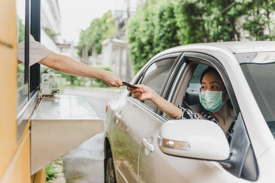 Woman in protective mask paying for fast food with credit card from her car.