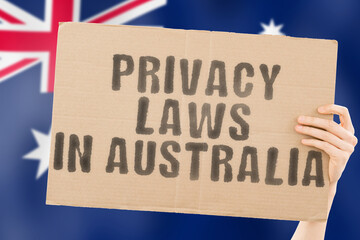 The phrase " Privacy laws in Australia " on a banner in men's hand with blurred Australian flag on the background. Private. Client. Market. Info. Information. Identify. Data. Security. Technology