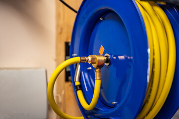 auto-rewinding air hose reel with coiled tubing mounted on a wall in a shop - obrazy, fototapety, plakaty