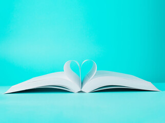 Love story book with open page of literature in heart shape on turquoise blue background. World Book Day, Teachers Knowledge. Minimal composition with copy space.
