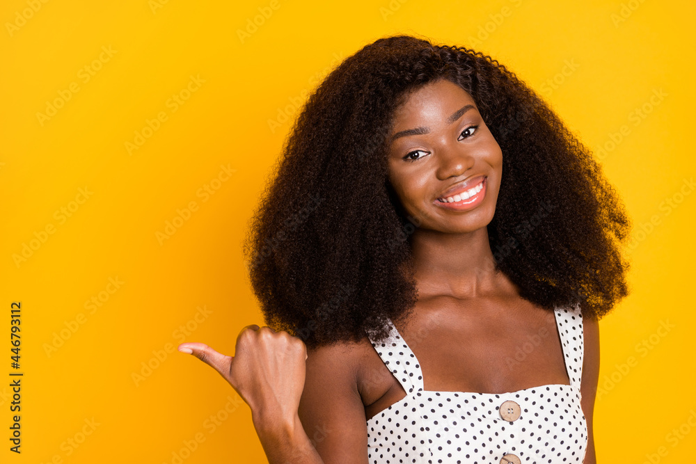 Sticker Photo of happy afro american lady point finger thumb empty space nice smile isolated on yellow color background