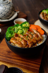 Japanese Food Style : Top view of Homemade Chicken Teriyaki grilled with rice , carrot , broccoli put on the black bowl and place on wooden table.