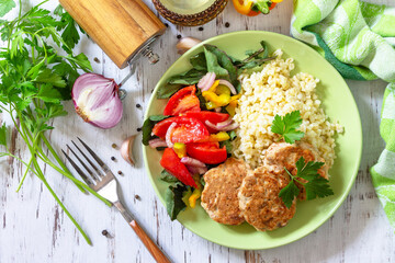 Healthy vegan food, keto or paleo diets. Homemade red fish cutlets with bulgur and fresh vegetable salad on a wooden table. Top view flat lay background.