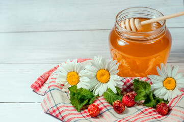 Obraz na płótnie Canvas honey in a transparent jar on a wooden background with daisies and strawberries. High quality photo