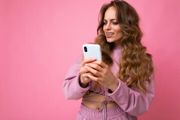 Beautiful amazed surprised blonde young woman wearing pink hoodie isolated over pink background...