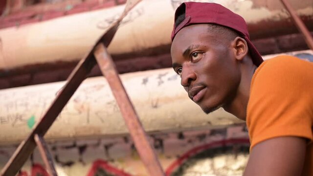 The camera zooms in on a young black guy sitting on a staircase in an alley in a dysfunctional neighborhood. Ghetto and young man. Slowmotion