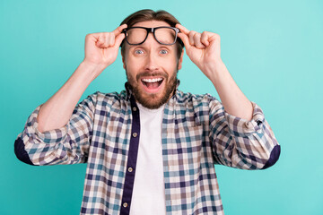 Photo of young man amazed shocked surprised hands touch eyeglasses news isolated over teal color background