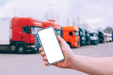 Mock up a smartphone in the hand of a man. Against the background of red trucks. Logistics concept.