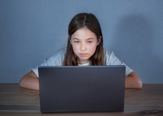 Naklejka premium a teenage girl is sitting at a table with a laptop late in social networks